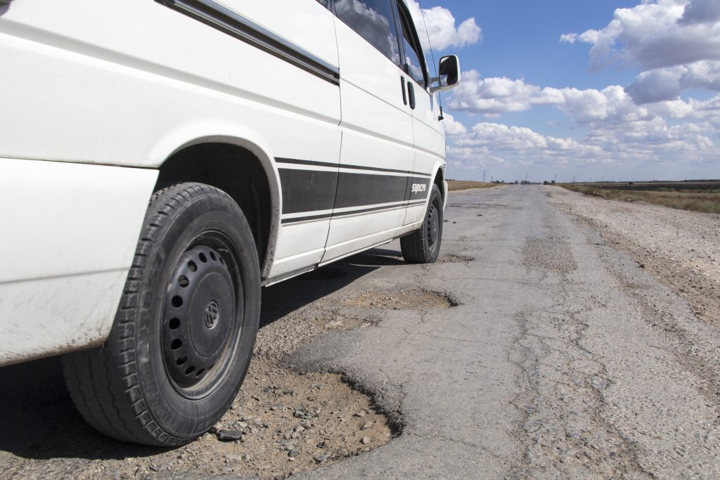 A white van over a pothole in the road